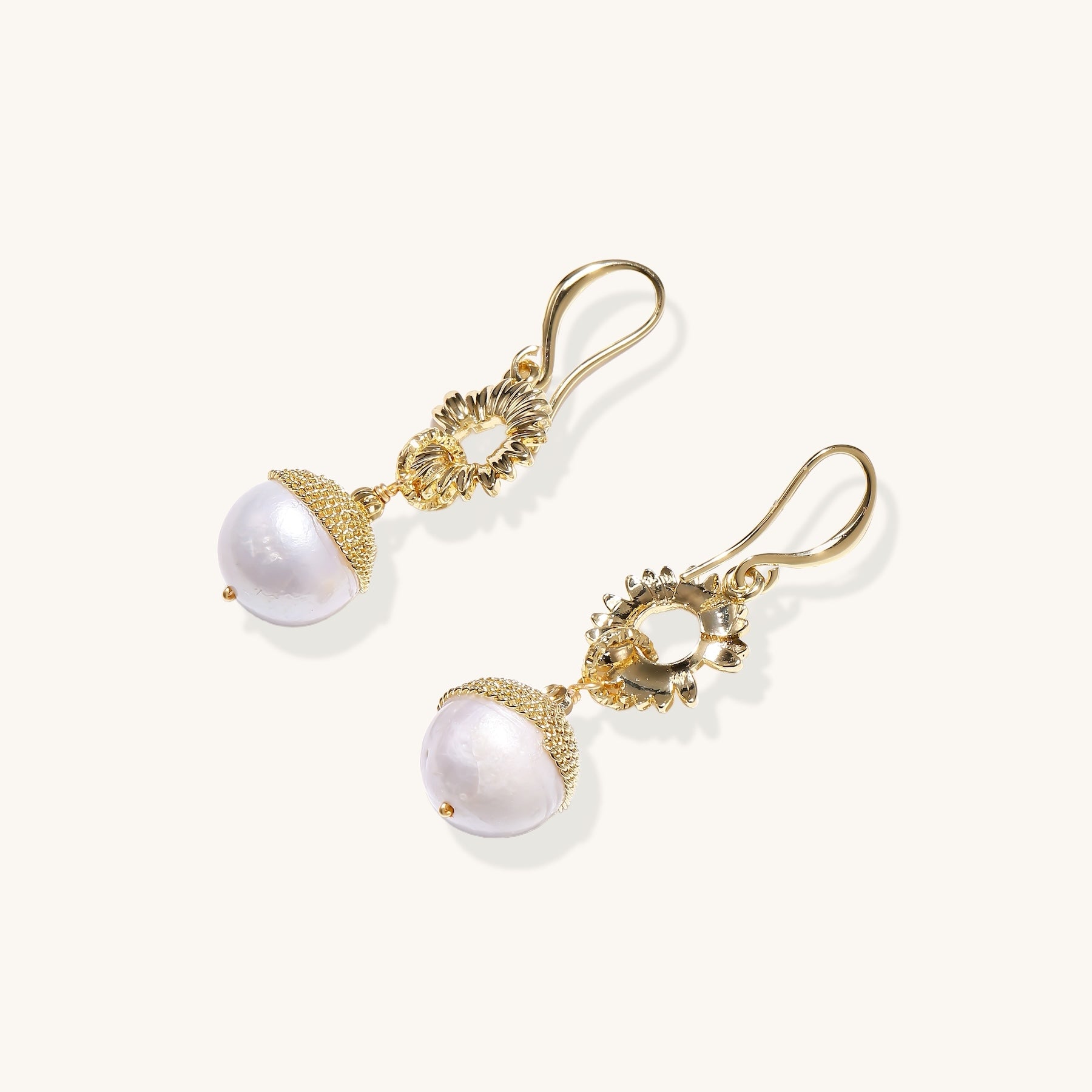 Gold-plated sunburst flower earrings with baroque pearl drops and textured metal caps on neutral background.