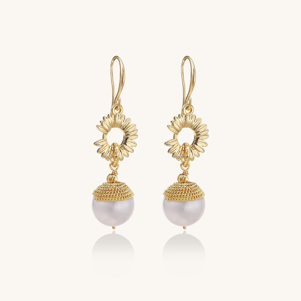 Gold-plated sunburst flower earrings with baroque pearl drops and textured metal caps on neutral background.
