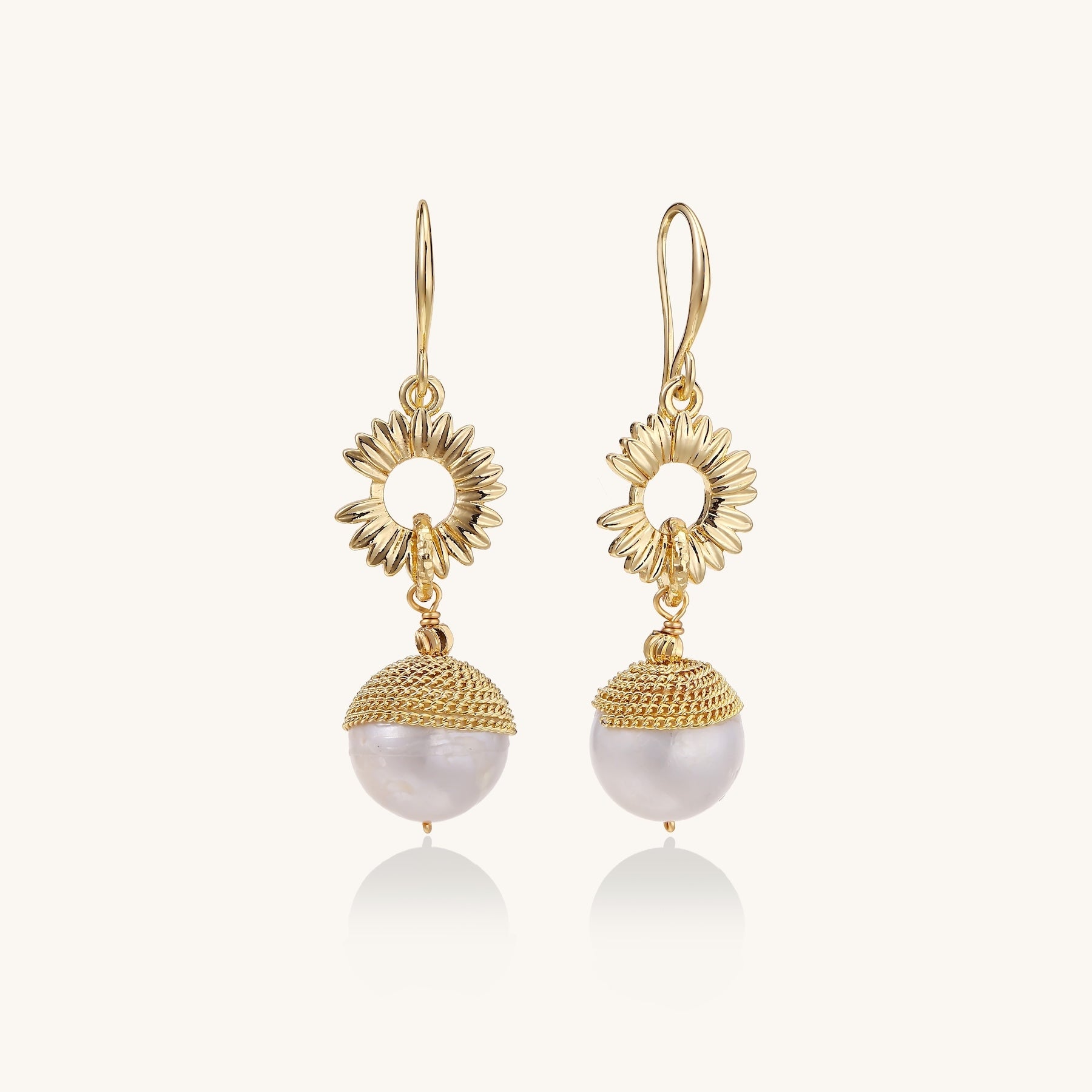 Gold-plated sunburst flower earrings with baroque pearl drops and textured metal caps on neutral background.