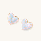 Heart-shaped stud earrings with iridescent blue-pink enamel finish and gold-plated brass frames against cream background