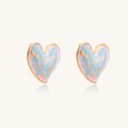 Heart-shaped stud earrings with iridescent blue-pink enamel finish and gold-plated brass frames against cream background