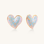 Heart-shaped stud earrings with iridescent blue-pink enamel finish and gold-plated brass frames against cream background