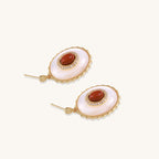 Gold-plated drop earrings with oval mother-of-pearl stones, central red gemstones, and crystal accents on white background.